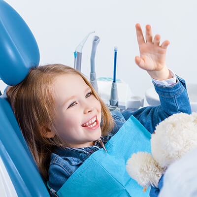 Kleines Mädchen sitzt mit Kuscheltier auf dem Zahnarztstuhl und lächelt