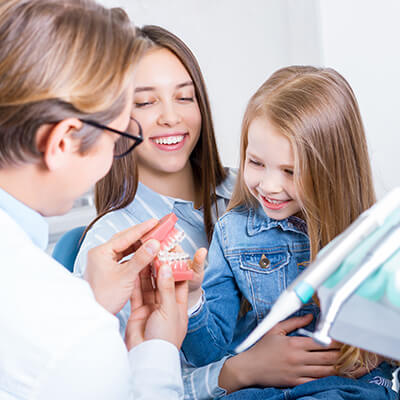 Mädchen sitzt bei Mutter auf dem Schoß beim Zahnarzt und betrachtet ein Gebiss